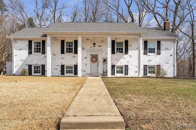 view of front of property with a chimney, roof with shingles, a front lawn, a porch, and brick siding