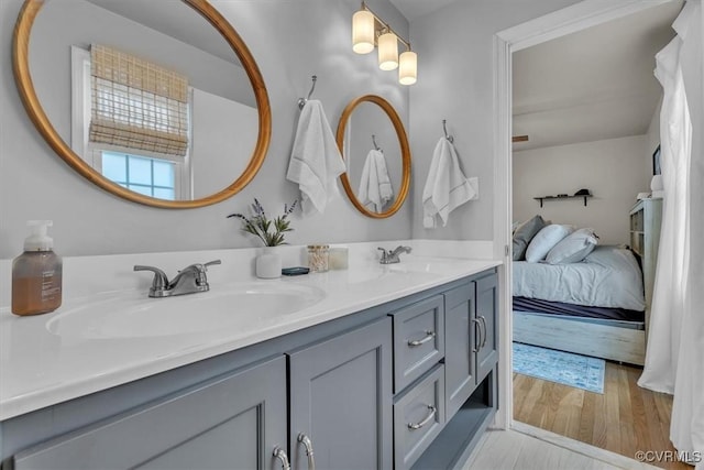 bathroom with double vanity, ensuite bath, a sink, and wood finished floors