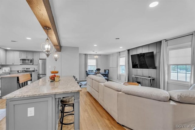 kitchen with appliances with stainless steel finishes, open floor plan, a breakfast bar area, gray cabinetry, and a notable chandelier