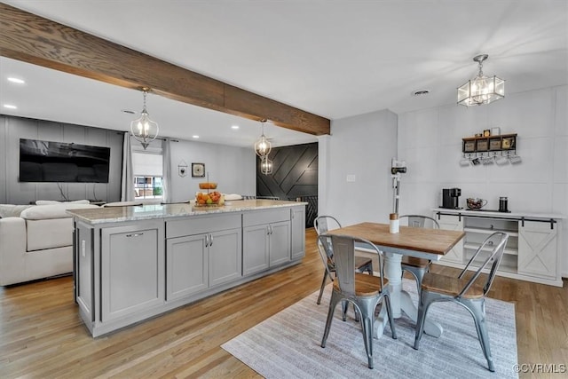 kitchen with gray cabinetry, open floor plan, hanging light fixtures, light wood-type flooring, and beamed ceiling