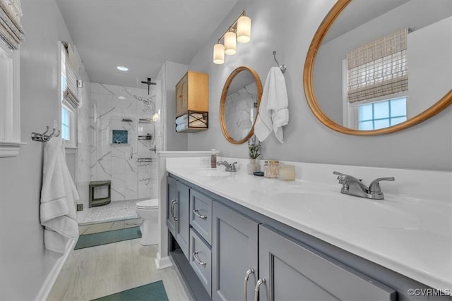 bathroom with a marble finish shower, double vanity, toilet, a sink, and baseboards