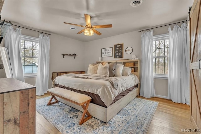 bedroom with a barn door, visible vents, baseboards, a ceiling fan, and light wood-type flooring