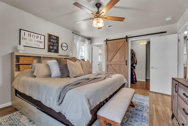 bedroom featuring visible vents, a barn door, light wood-style floors, ceiling fan, and baseboards