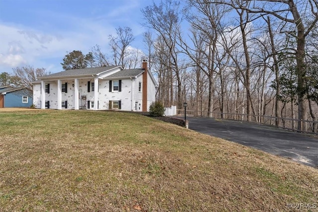 view of front of home with covered porch, a chimney, and a front lawn