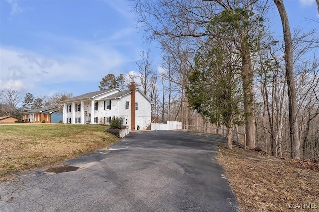 view of home's exterior with aphalt driveway, a lawn, a chimney, and fence