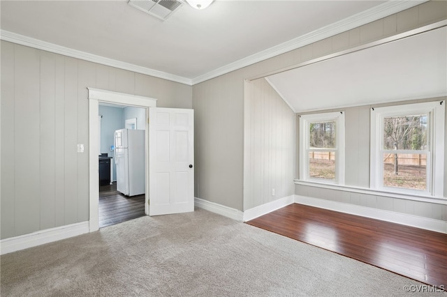 carpeted spare room featuring baseboards, wood finished floors, visible vents, and crown molding