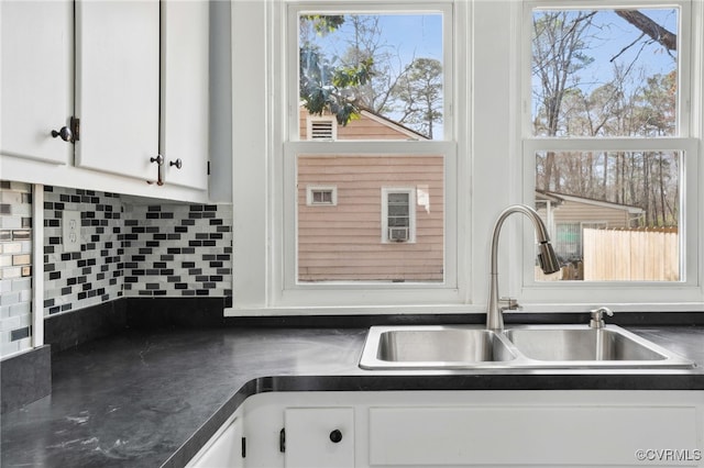 kitchen with backsplash, dark countertops, a sink, and white cabinetry