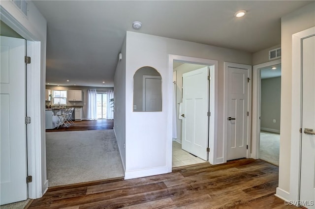 hallway with carpet floors, visible vents, baseboards, and wood finished floors