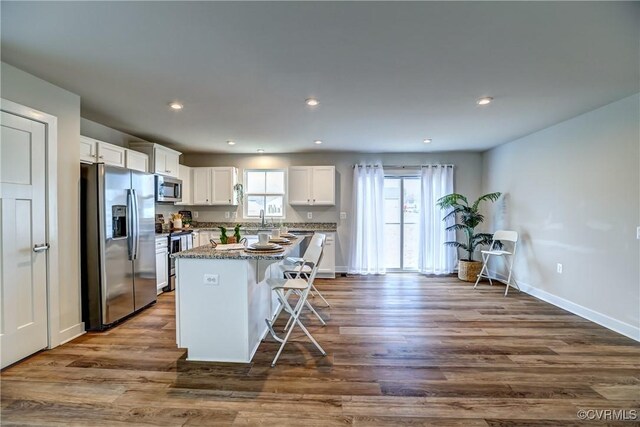 kitchen with dark wood-type flooring, a sink, a kitchen island, white cabinets, and appliances with stainless steel finishes