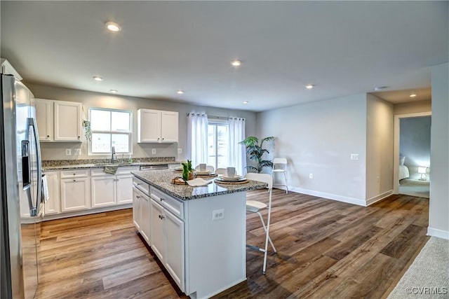 kitchen with a breakfast bar area, white cabinets, a kitchen island, dark stone countertops, and stainless steel fridge