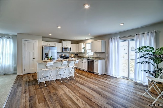 kitchen with wood finished floors, a sink, white cabinetry, appliances with stainless steel finishes, and a center island