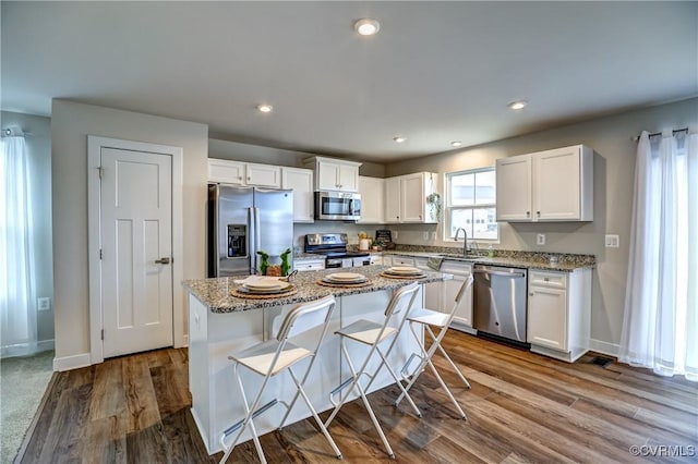 kitchen featuring dark wood finished floors, a kitchen island, light stone counters, stainless steel appliances, and white cabinetry