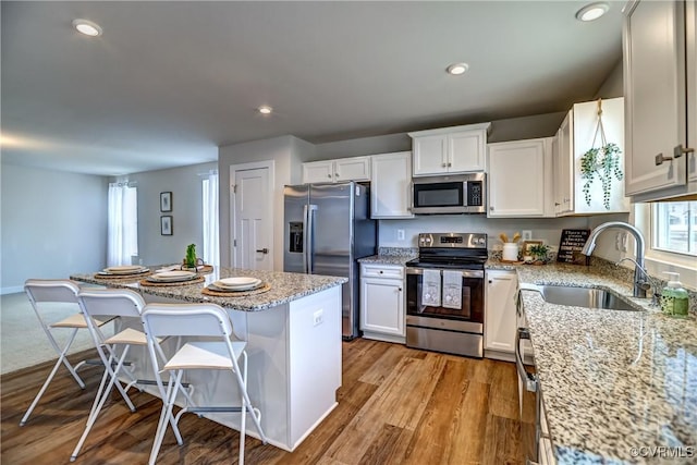 kitchen with stainless steel appliances, a kitchen island, a sink, white cabinets, and light wood finished floors