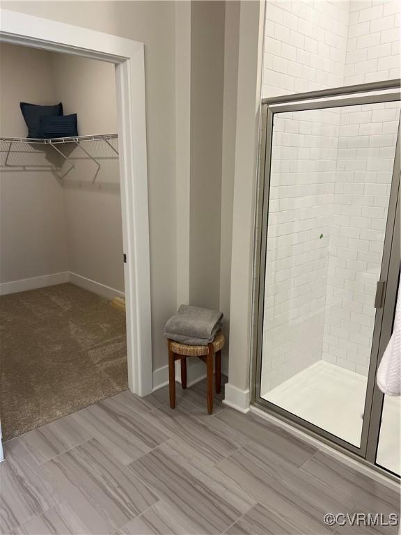 full bathroom featuring baseboards, a spacious closet, and a shower stall