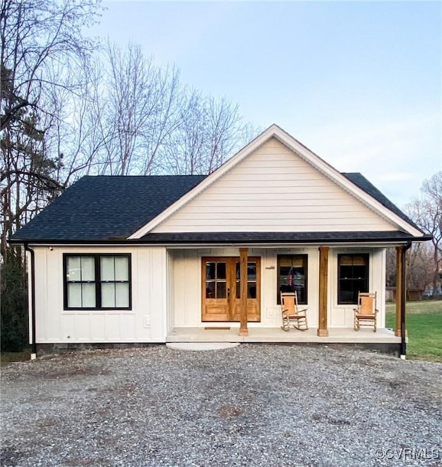 view of front of property featuring covered porch, roof with shingles, board and batten siding, and gravel driveway