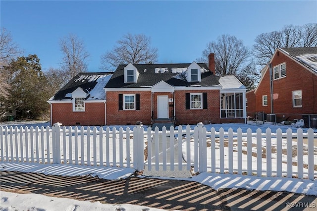 view of front of home featuring brick siding, a chimney, a fenced front yard, and a sunroom