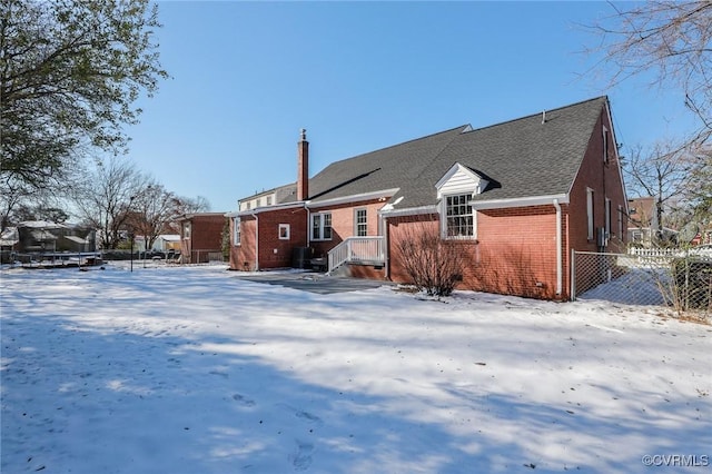 snow covered rear of property with fence and brick siding