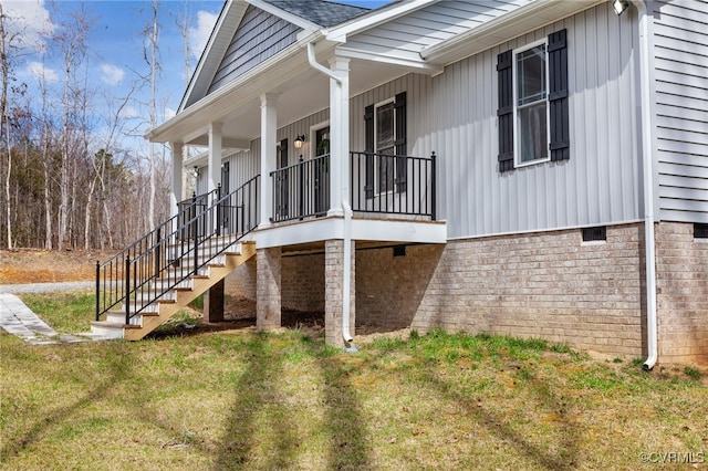 view of side of property with crawl space, covered porch, a lawn, and stairs