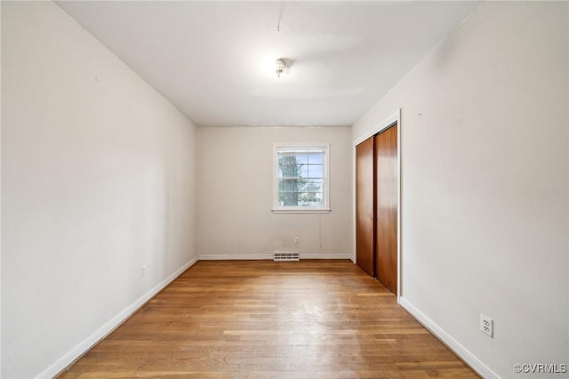 unfurnished bedroom with a closet, baseboards, visible vents, and wood finished floors