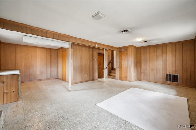 unfurnished room featuring visible vents, light floors, wood walls, and stairway