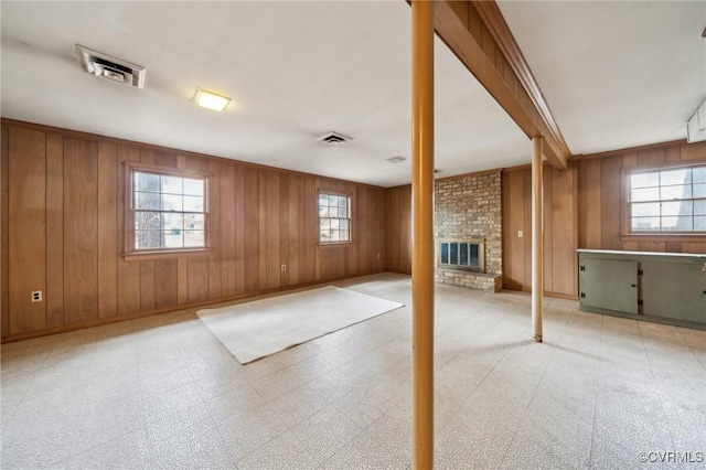 below grade area with a fireplace, wooden walls, light floors, and visible vents