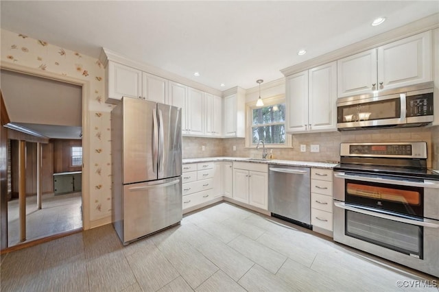 kitchen with light stone countertops, a sink, decorative backsplash, appliances with stainless steel finishes, and decorative light fixtures