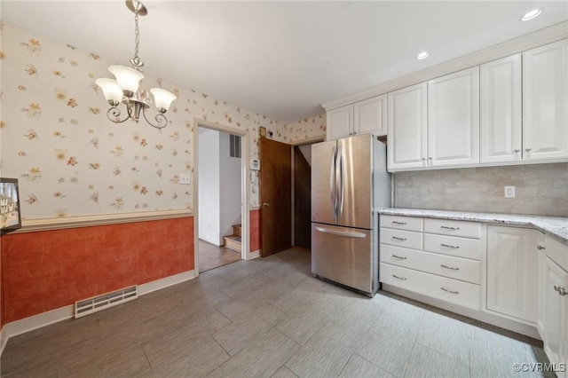 kitchen with visible vents, wallpapered walls, wainscoting, freestanding refrigerator, and white cabinets