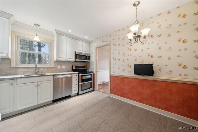 kitchen with a wainscoted wall, a sink, appliances with stainless steel finishes, white cabinets, and wallpapered walls