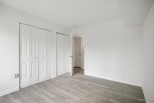 unfurnished bedroom featuring wood finished floors, multiple closets, and baseboards