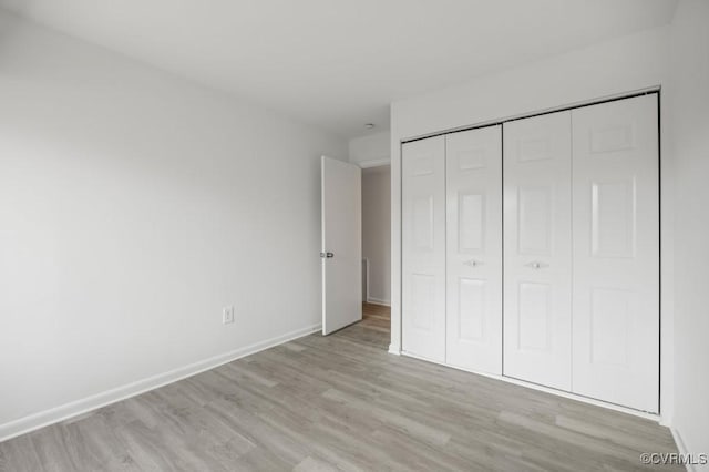 unfurnished bedroom with light wood-style flooring, baseboards, and a closet