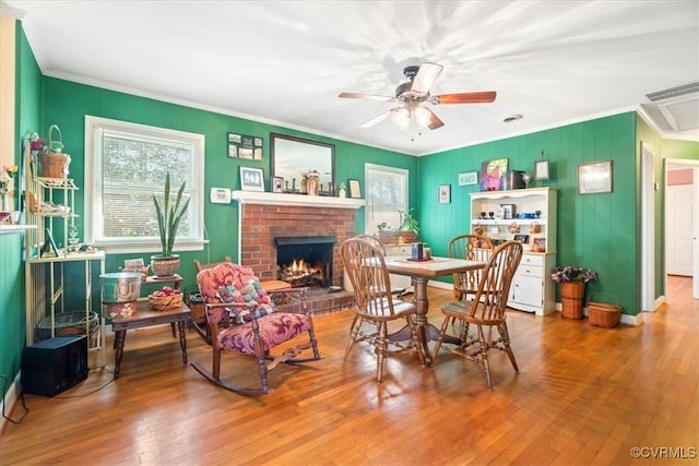 dining space with visible vents, a ceiling fan, hardwood / wood-style floors, crown molding, and a brick fireplace