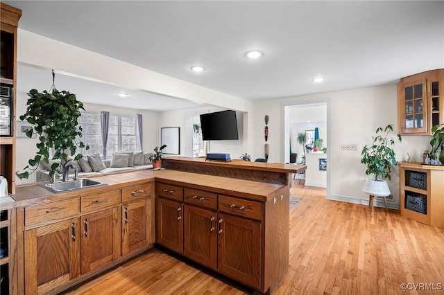 kitchen featuring light wood-type flooring, brown cabinets, a sink, open floor plan, and tile countertops