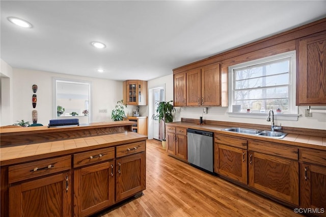 kitchen featuring a sink, stainless steel dishwasher, tile countertops, brown cabinetry, and light wood finished floors