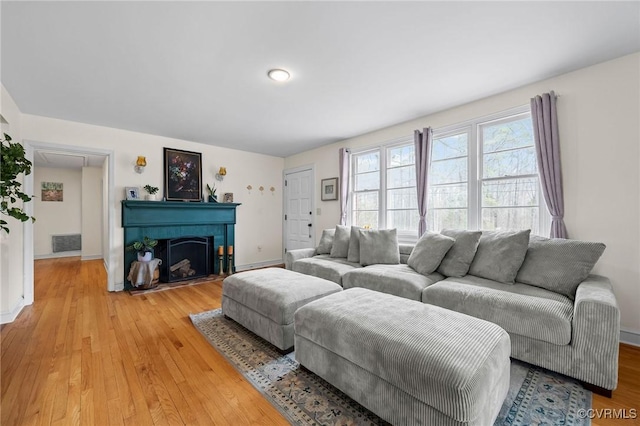 living area with a fireplace with flush hearth, baseboards, visible vents, and light wood finished floors