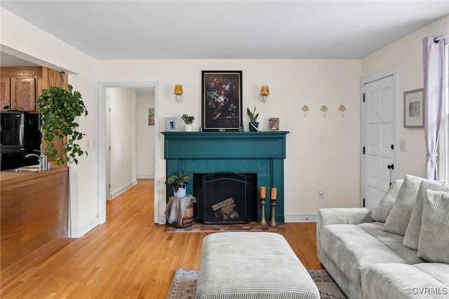 living room with baseboards, a brick fireplace, and light wood finished floors