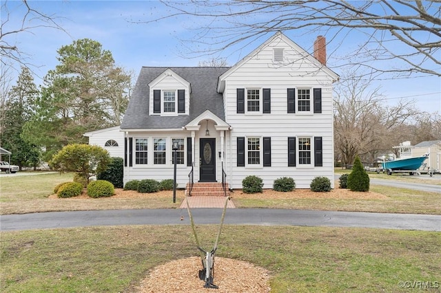 view of front of home with a front lawn, roof with shingles, and a chimney