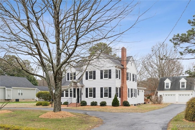 colonial-style house with a front lawn, a detached garage, and a chimney