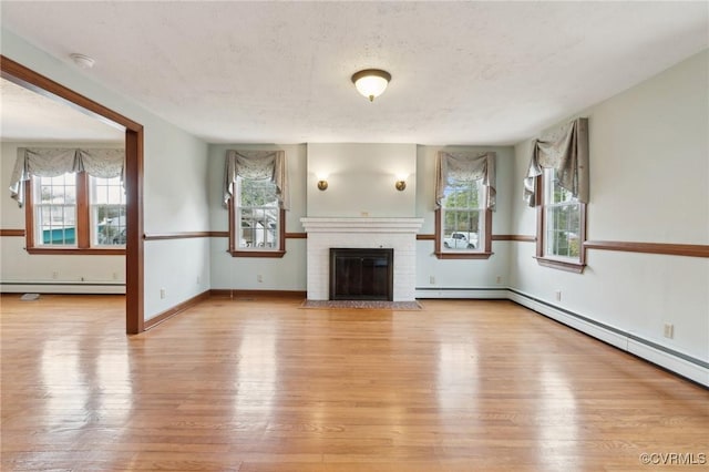 unfurnished living room with a baseboard radiator, baseboards, wood finished floors, and a fireplace