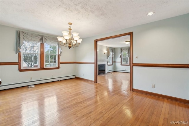 spare room with a chandelier, baseboard heating, light wood finished floors, and a wealth of natural light