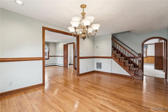 unfurnished room featuring visible vents, stairway, arched walkways, light wood finished floors, and a chandelier