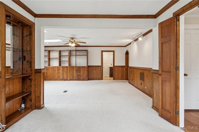 empty room with light carpet, wainscoting, a ceiling fan, and ornamental molding