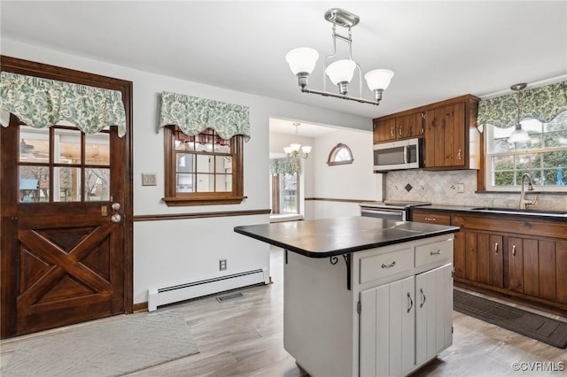 kitchen featuring a sink, appliances with stainless steel finishes, a baseboard heating unit, dark countertops, and a notable chandelier