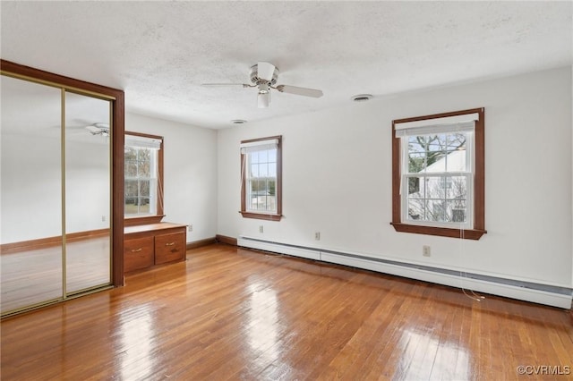 unfurnished bedroom with a baseboard heating unit, baseboards, hardwood / wood-style flooring, a closet, and a textured ceiling