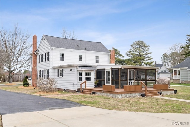 back of property featuring a deck, driveway, a sunroom, and a chimney