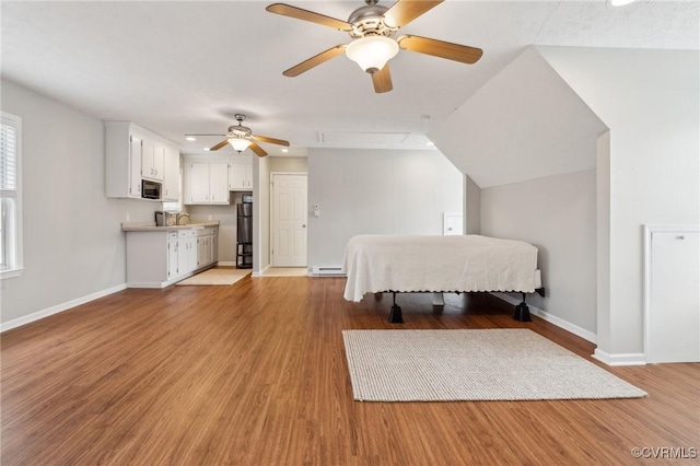 bedroom featuring a ceiling fan, baseboards, a baseboard radiator, light wood-style flooring, and refrigerator