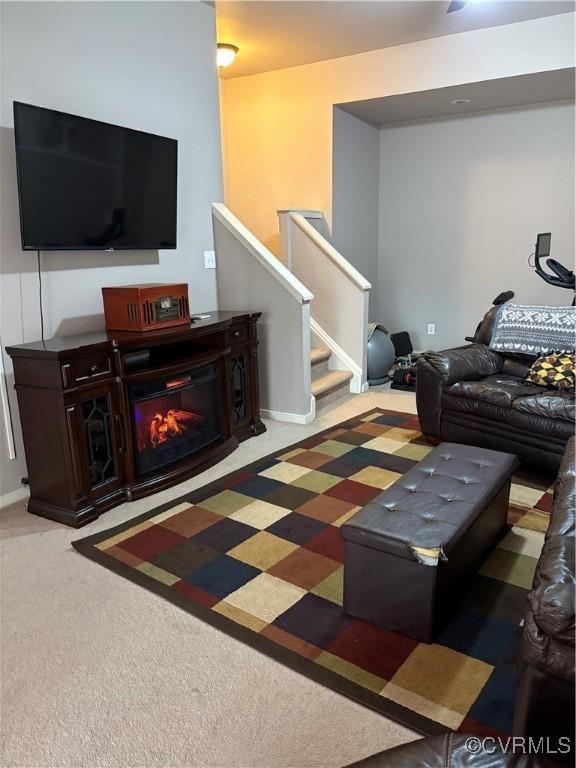 carpeted living room featuring a glass covered fireplace, stairway, and baseboards