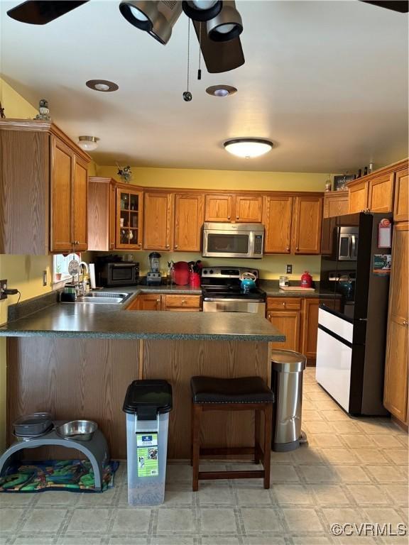 kitchen with light floors, a peninsula, a sink, stainless steel appliances, and brown cabinets