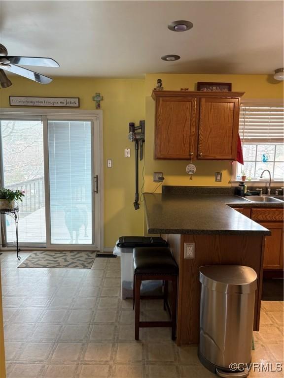 kitchen with a breakfast bar area, light floors, ceiling fan, a sink, and dark countertops