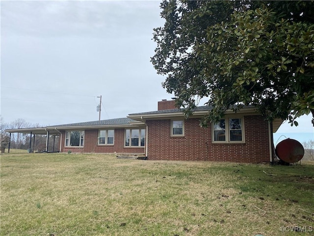 back of house featuring brick siding, a chimney, and a yard