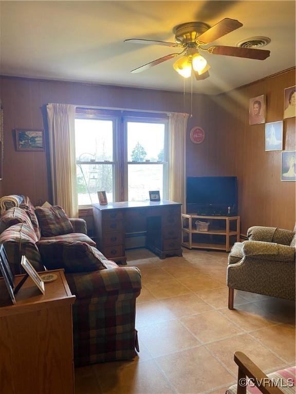 living area with light tile patterned flooring, a ceiling fan, visible vents, and wood walls